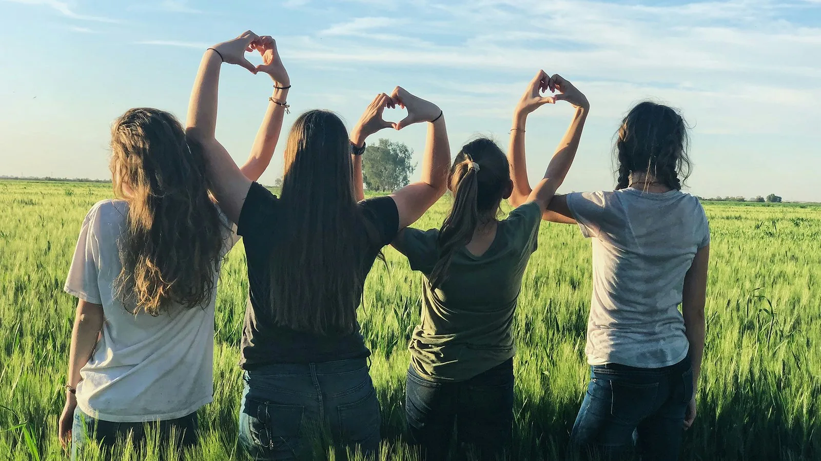 Jóvenes en un campo formando corazones con los brazos